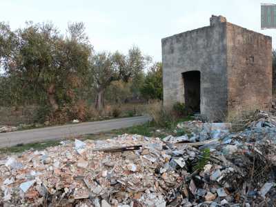 La viuzza, delimitata da bassi muretti a secco, si inoltra tra vasti uliveti puntellati dalla solita sporcizia. Sulla destra, davanti a un piccolo rudere, balza all'occhio un cumulo di immondizia spaventoso...